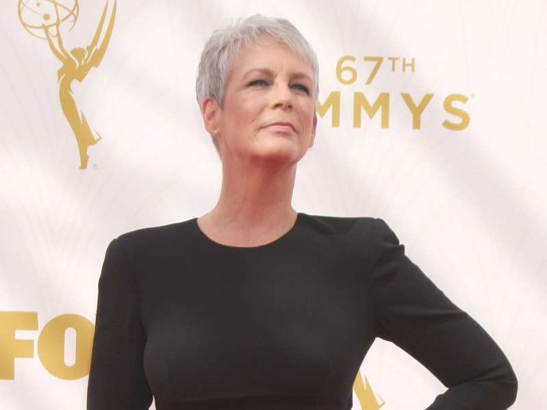 Jamie Lee Curtis smiles with a hand on her hip. She is wearing a long-sleeved black dress