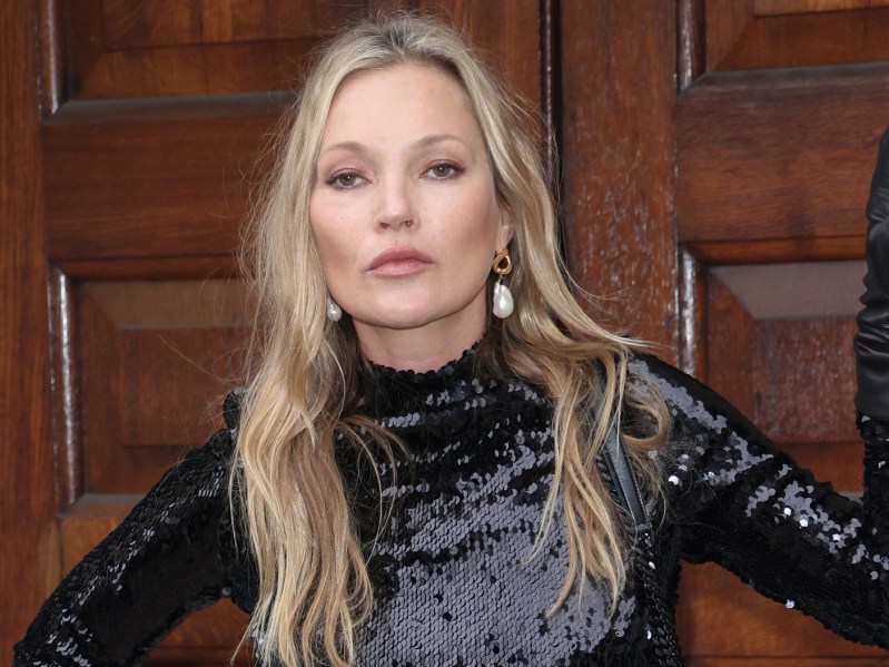 Kate Moss poses in long-sleeved black dress in front of wooden door