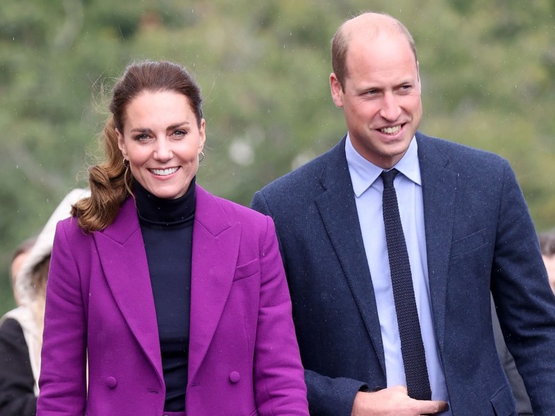 Kate Middleton (L) in purple pantsuit standing next to Prince William, who is wearing a navy blue suit and tie