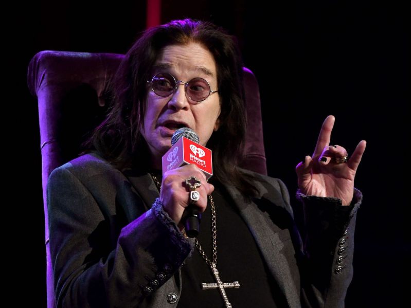 2020 photo of Ozzy Osbourne in a black and grey outfit speaking into a microphone while sitting on stage
