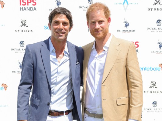 Prince Harry (R) in tan suit standing next to Nacho Figueras, who is wearing a gray suit