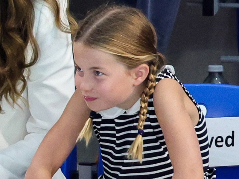 Princess Charlotte hunches in her seat and grins. She is wearing a black and white striped polo dress