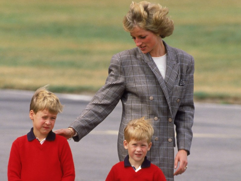Princess Diana (R) guides young Princes Harry and William outside, both of whom are wearing red sweaters