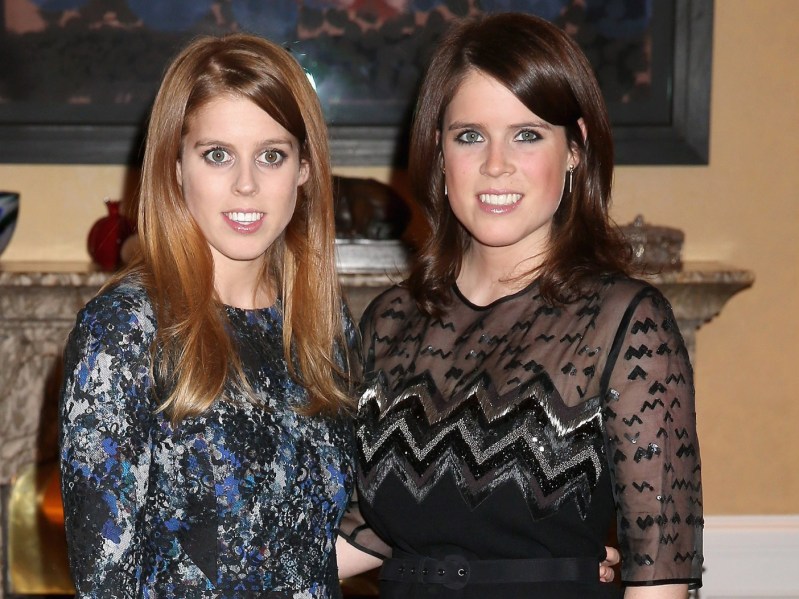 Princess Beatrice (L) in blue dress standing next to Princess Eugenie in a black dress