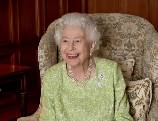 Queen Elizabeth in a green blouse smiling while sitting in an armchair