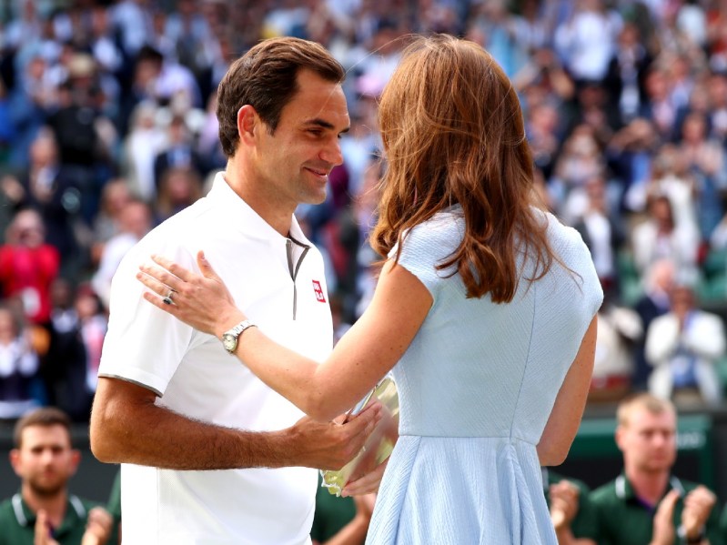 Roger Federer (L) in white shirt standing across from Kate Middleton, who is seen from behind wearing baby blue dress