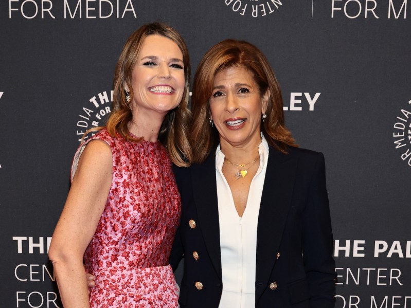 Savannah Guthrie in a red dress smiling with Hoda Kotb in a black pantsuit