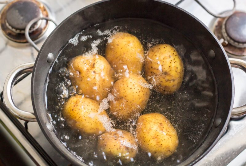 Pot on stove boiling small whole potatoes.
