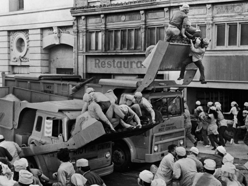 Black and white photo of multiple tanks with people hanging off of them and jumping off