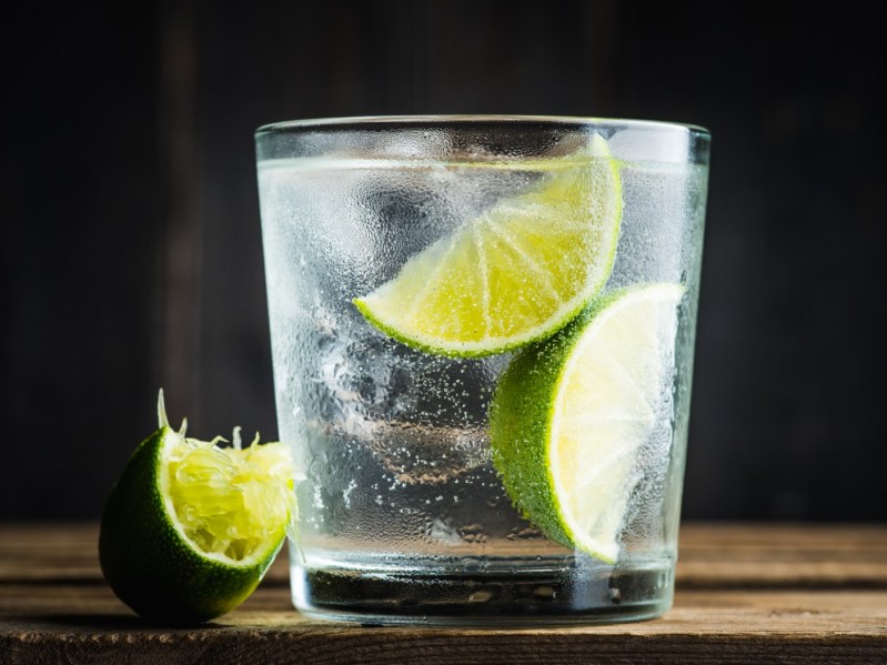 Closeup image of a vodka soda cocktail with a slice of lime next to it