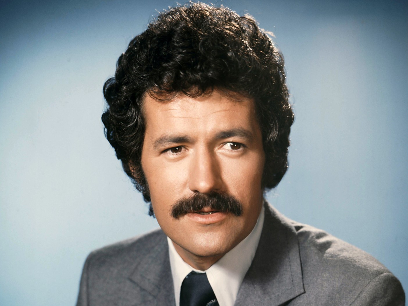 Portrait of a young Alex Trebek against sky blue backdrop