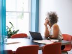 woman with gray curly hair looks out window sitting at desk