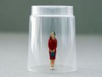 Female figurine standing under overturned glass cup