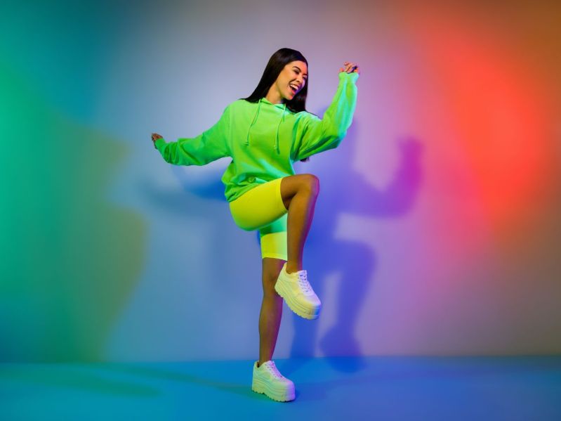 woman with long straight hair wearing bright colors dances and smiles