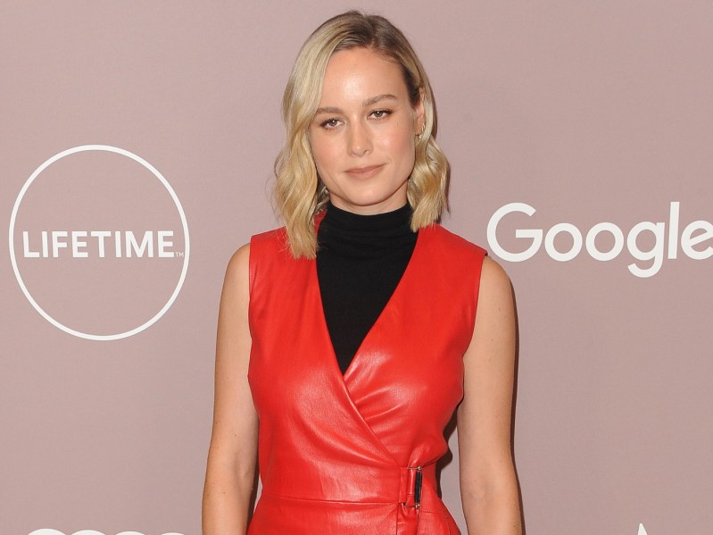 Brie Larson poses in red leather vest over black sleeveless turtleneck