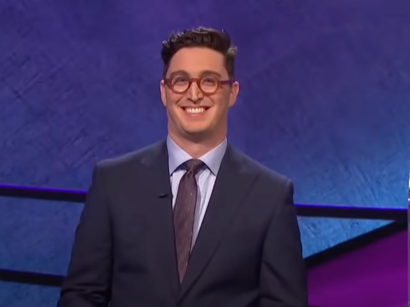 Buzzy Cohen smiles in navy blue suit with burgundy tie