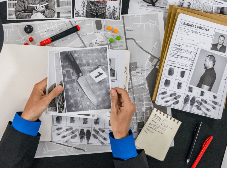 stock image of a pair of hands holding a crime scene photo above a desk scattered with case files