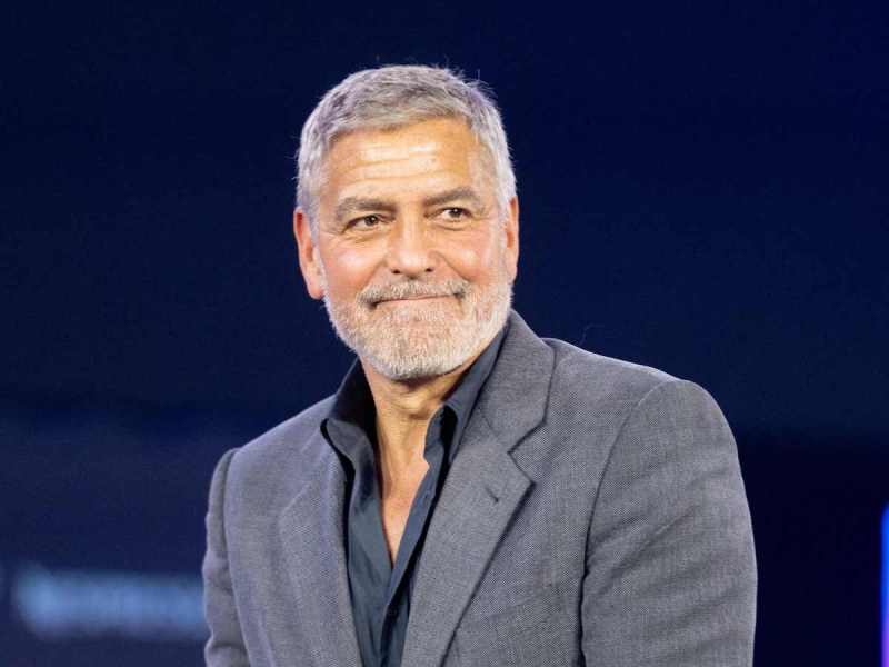 George Clooney smiling in a grey suit on stage