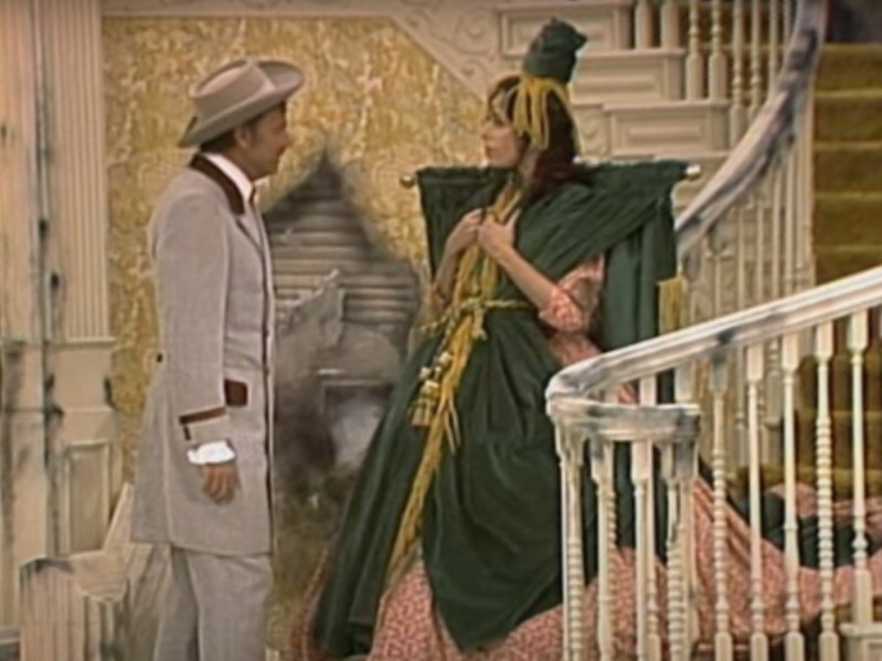 Carol Burnett (R) in green curtain-rod dress standing across from man in a gray suit
