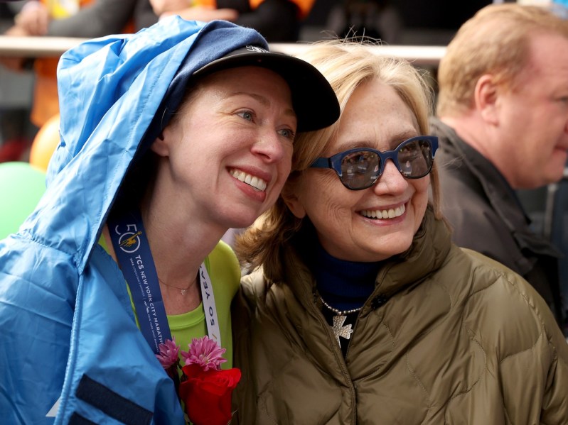 Chelsea Clinton (L) in blue rain jacket posing with Hillary Clinton, who is wearing a green jacket and sunglasses