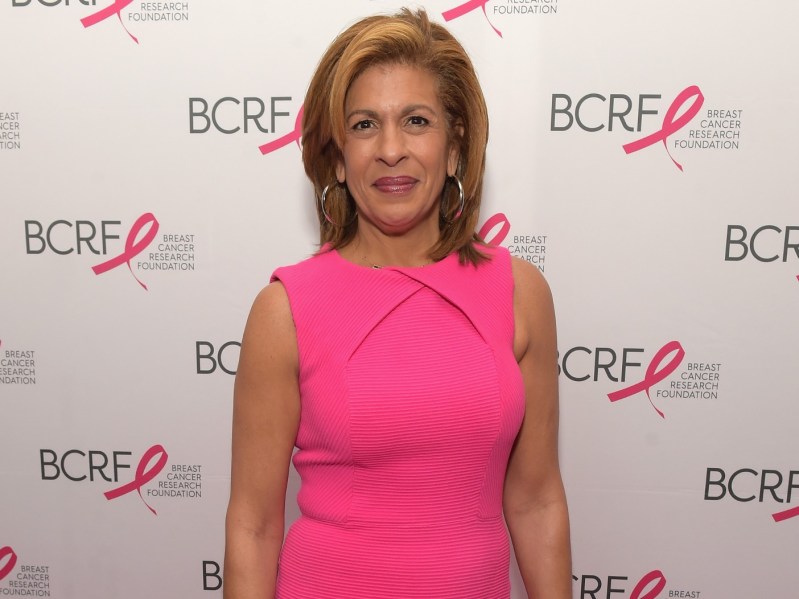 Hods Kotb smiles in pink dress against white backdrop