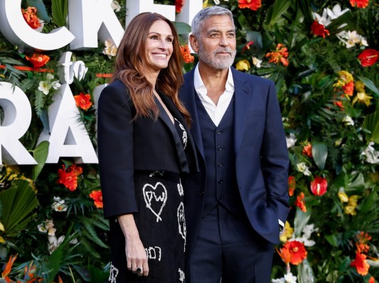 Julia Roberts (L) and George Clooney standing in front of wall of greenery and flowers