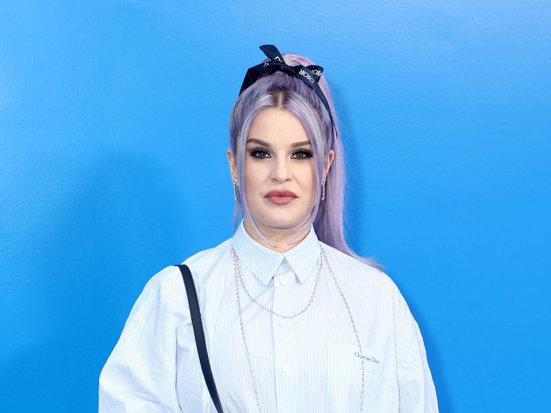 Kelly Osbourne in a white blouse against a blue background