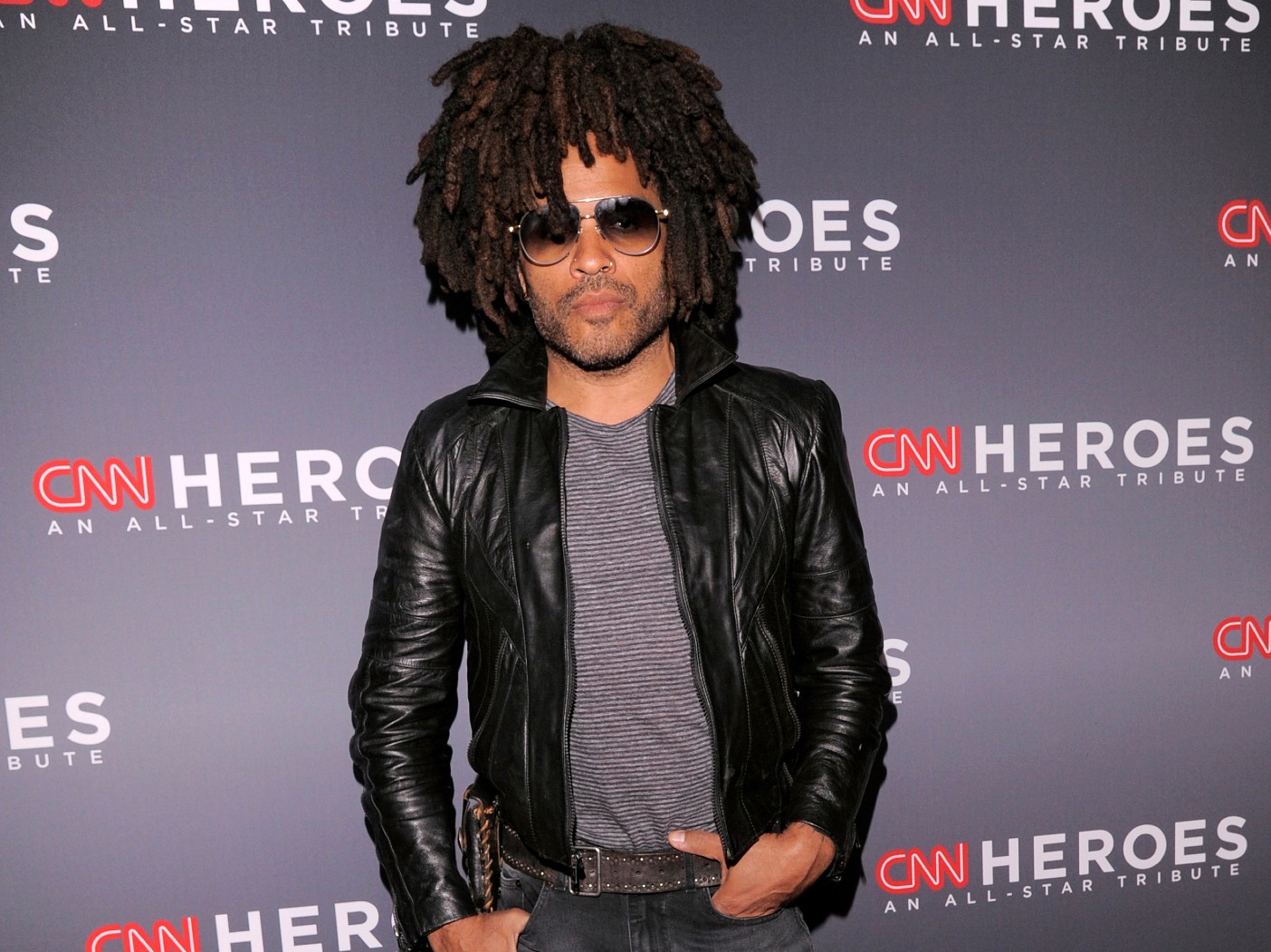 Lenny Kravitz poses with black leather jacket over gray shirt