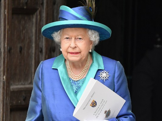 Queen Elizabeth leaves a building while wearing a blue blazer and matching hat
