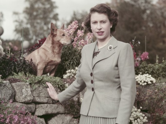 A young Queen Elizabeth poses with her dog outside in a garden