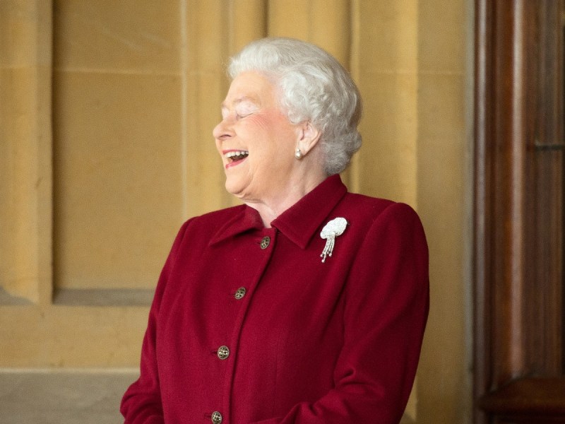 Queen Elizabeth laughing in dark red jacket with brooch
