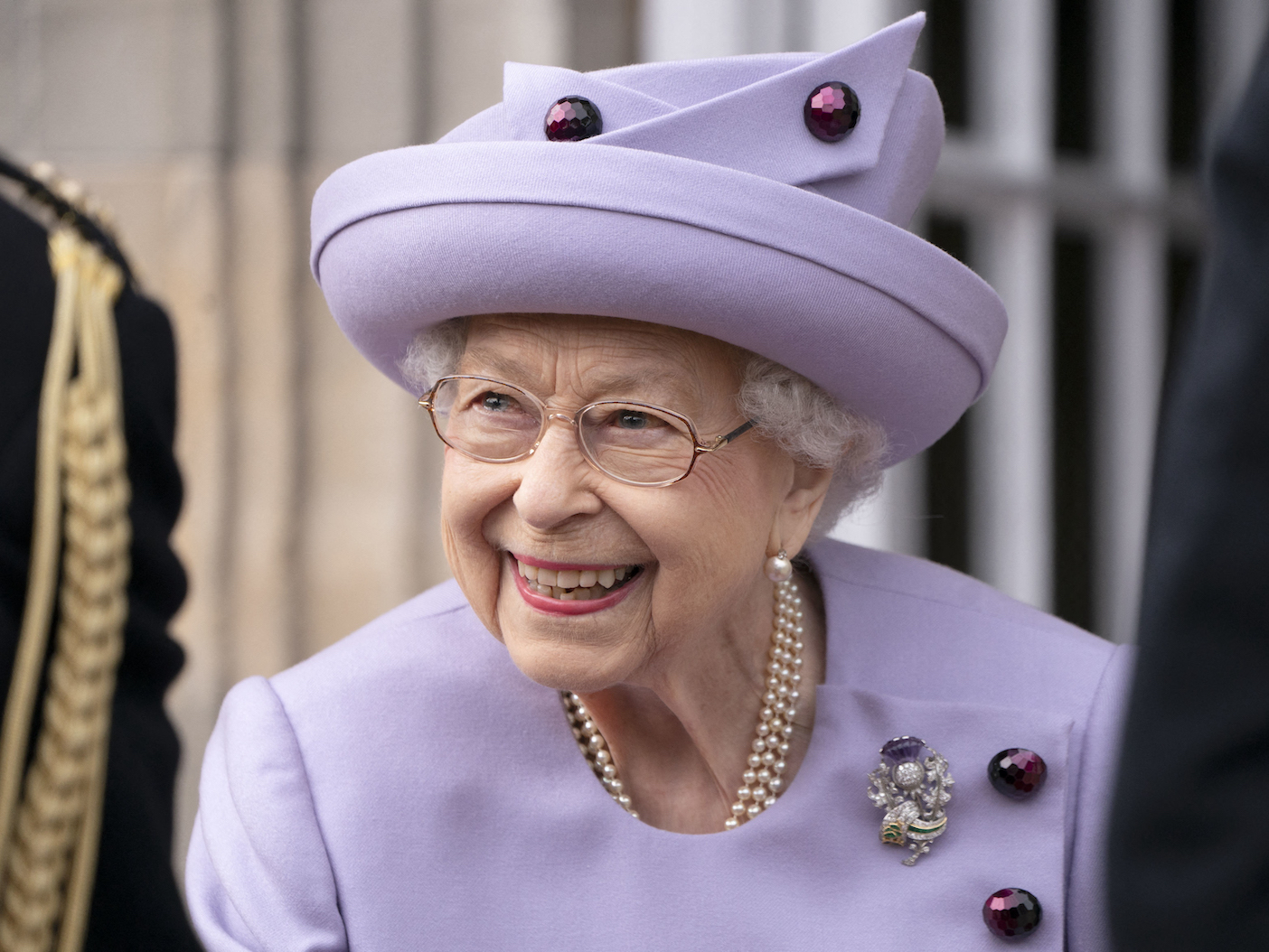 closeup photo of Queen Elizabeth smiling in a purple outfit and hat