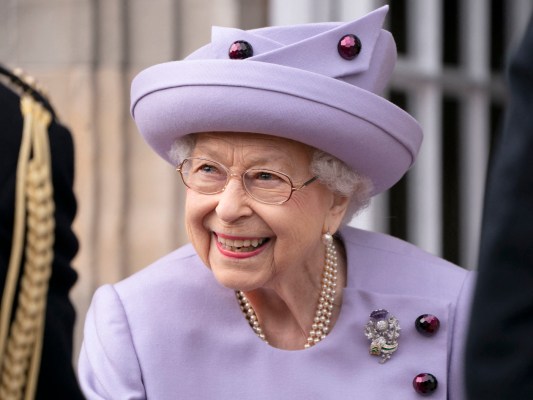 closeup photo of Queen Elizabeth smiling in a purple outfit and hat