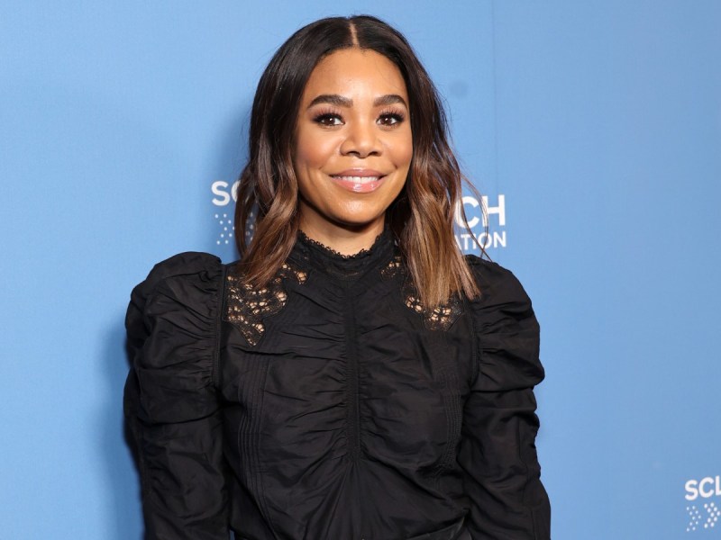 Regina Hall smiles in black blouse against blue backdrop