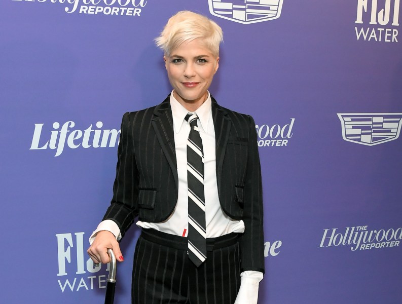 Selma Blair in a black suit and tie smiling with platinum blonde hair