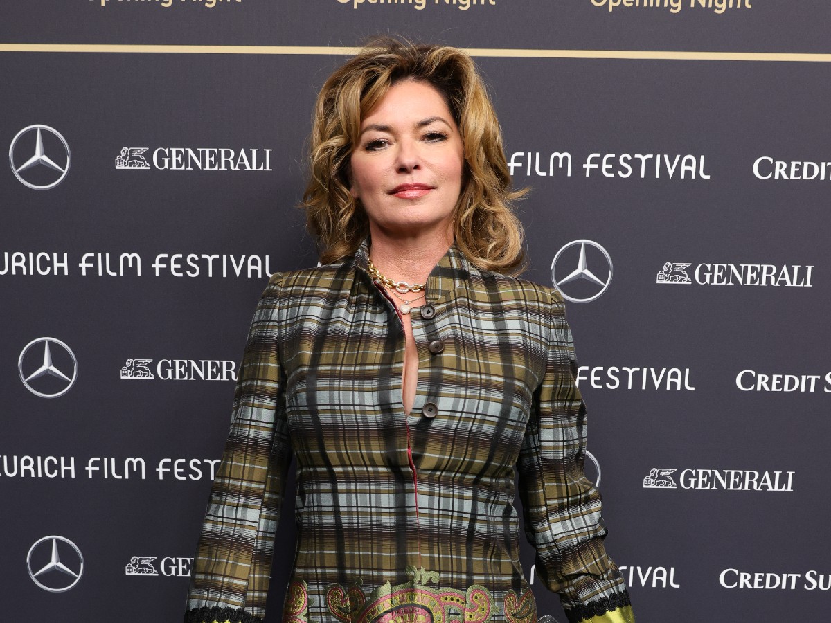 Shania Twain smiles in black and green and gray plaid top