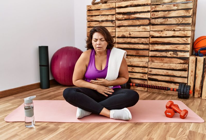 Woman sitting on a yoga mat holding her stomach in pain
