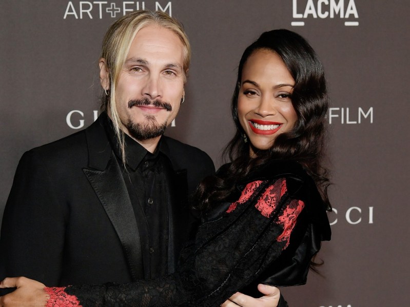 Zoe Saldana (R) with husband Marco standing against gray/brown backdrop