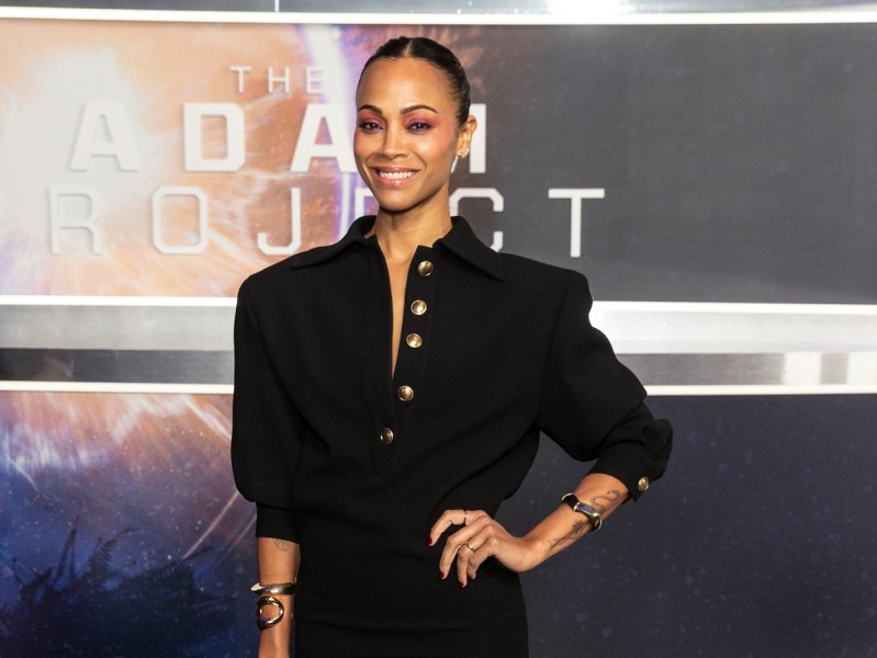 Zoe Saldana smiling in a black dress with hand on hip