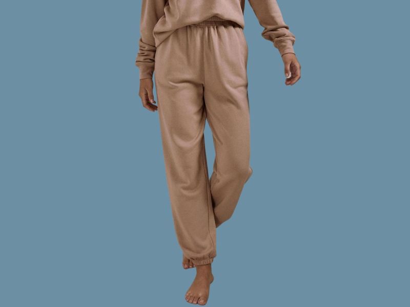 Lower half of a woman wearing tan sweatpants and sweatshirt on a blue background