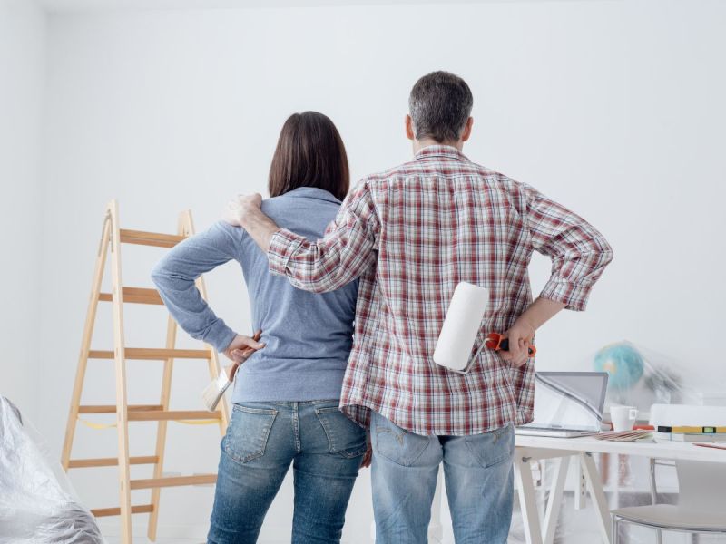 Man and woman hold painting tools and look at blank wall