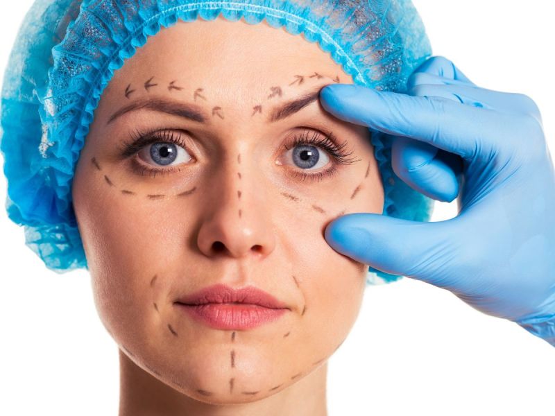 Woman with plastic surgery marks on face, hand with medical glove touching face