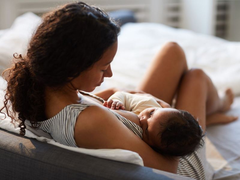 A woman with dark curly hair breast feeds her baby.