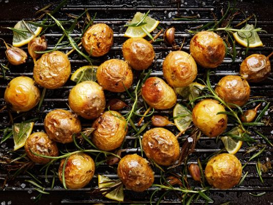 Roasted potatoes and various herbs and seasonings lying on a black background
