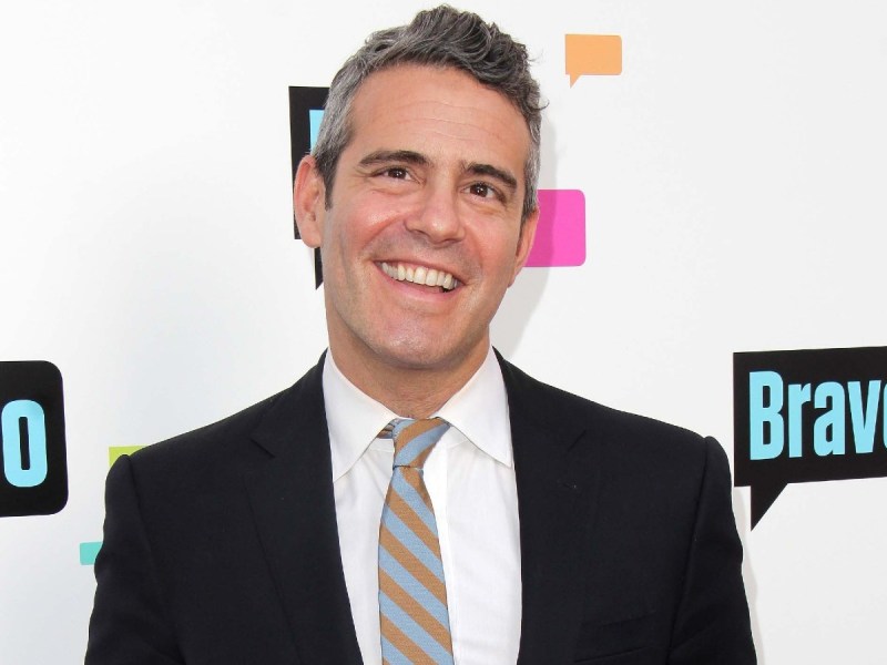 Andy Cohen smiles in white dress shirt with black suit and striped necktie