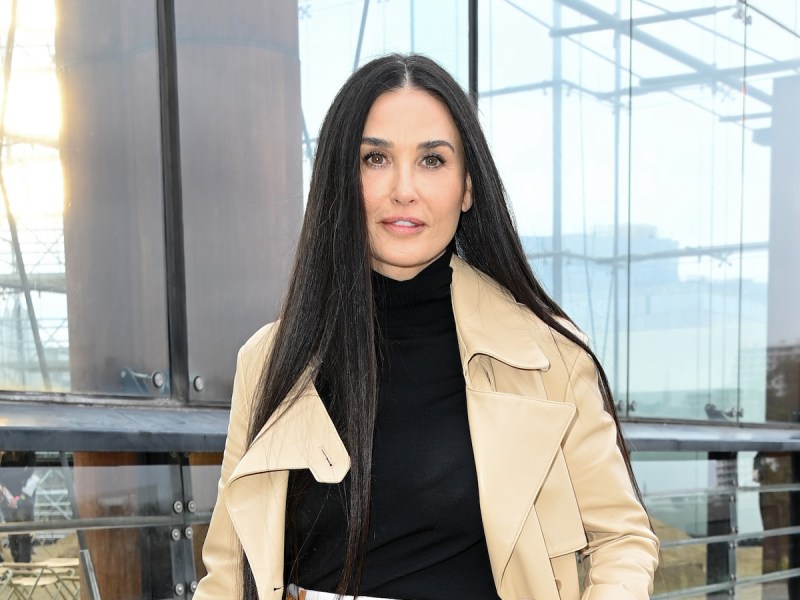 Demi Moore smiling in a black sweater and tan coat