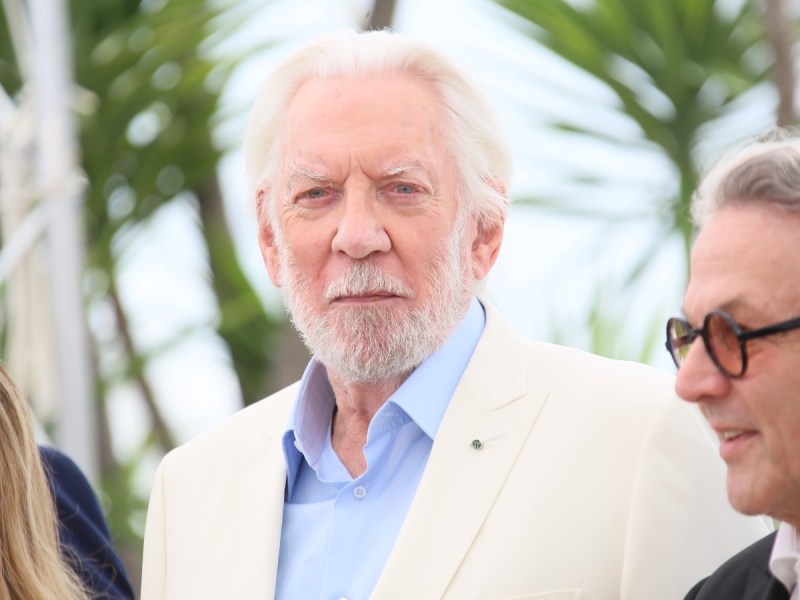 Donald Sutherland looks ahead in blue dress shirt with cream-colored blazer