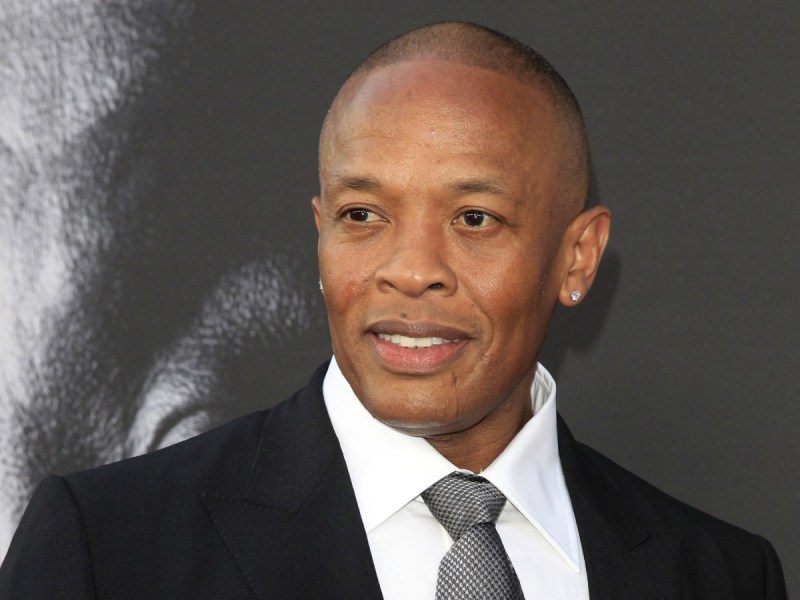 Dr. Dre poses in black jacket with gray tie against gray backdrop