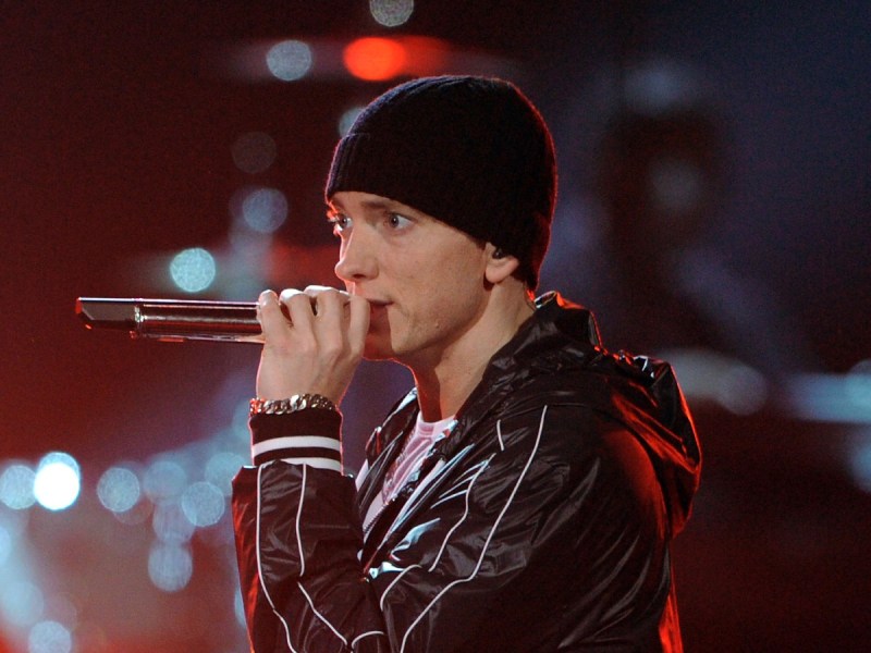 Eminim raps into a microphone onstage while wearing a leather jacket and black sock hat