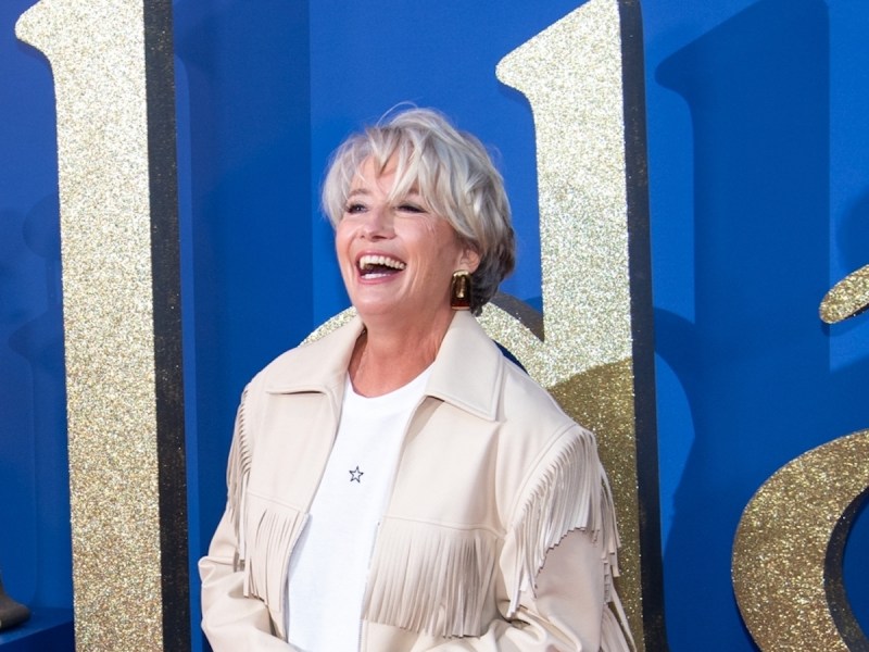 Emma Thompson laughing in a tan coat and white jumper